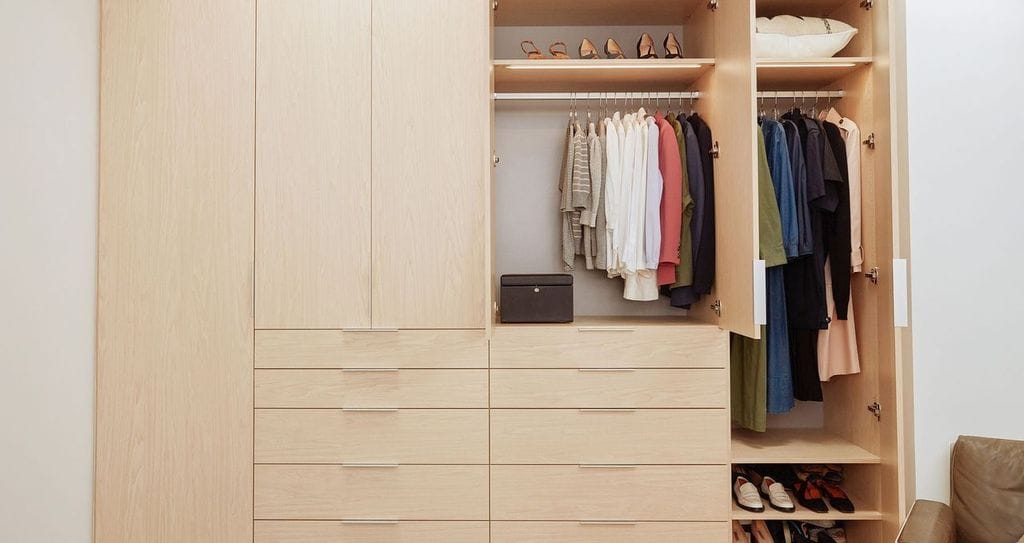 Wardrobe closet with custom cabinets and drawers designed in a natural wood grain finish by California Closets
