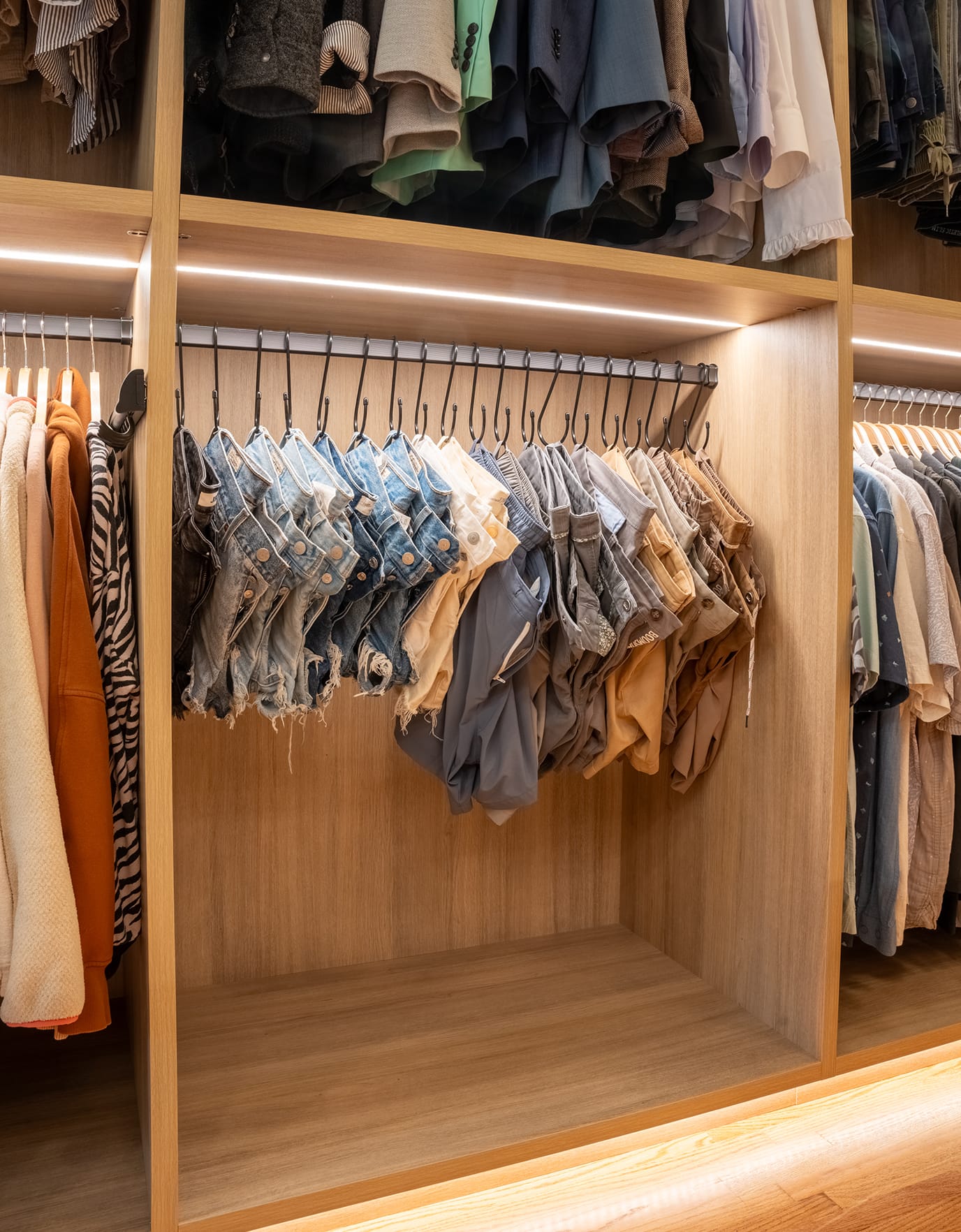 Walk in closet designed to hang everything up with hook hangers for denim and LED lighting to easily find items by California Closets