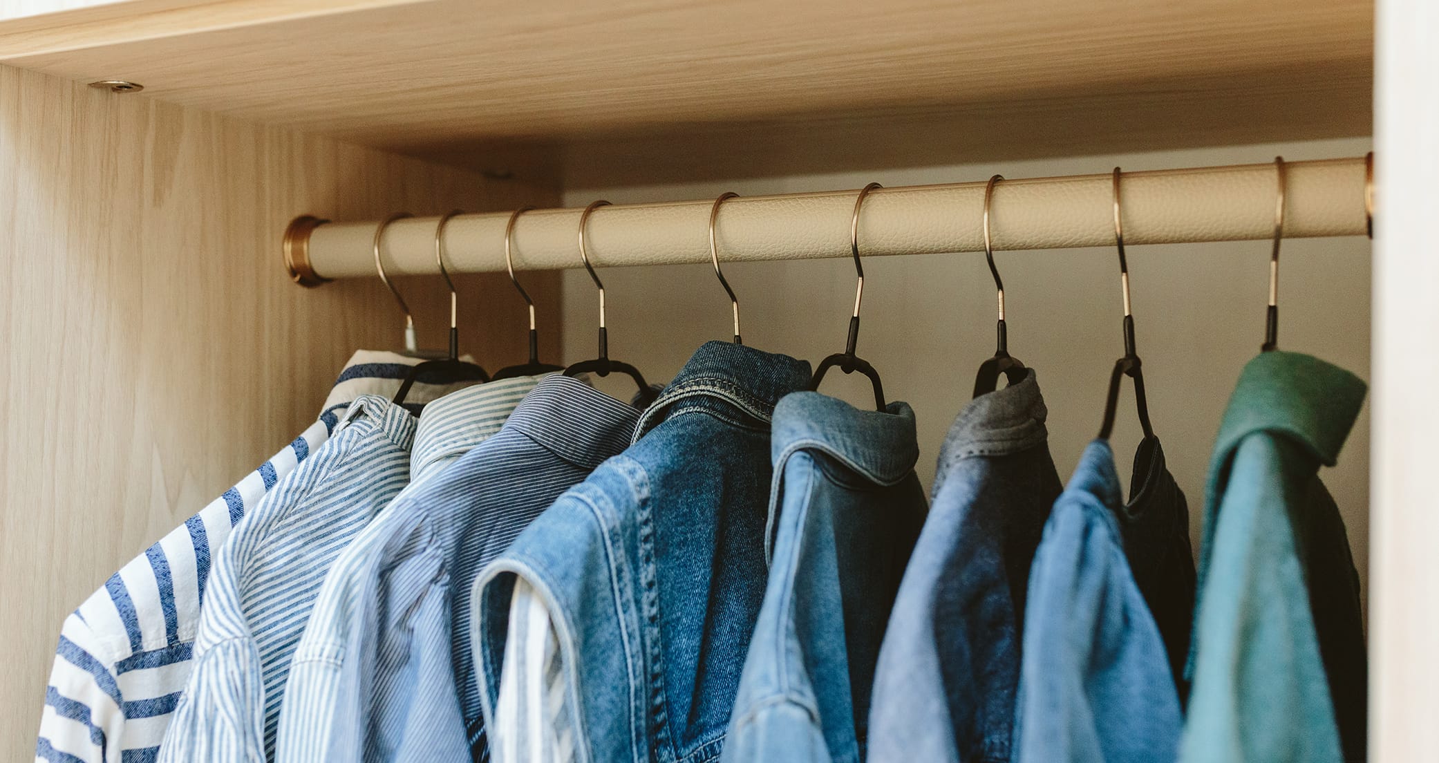 Close up of walk in closet custom wood grain finish clothes pole by California Closets