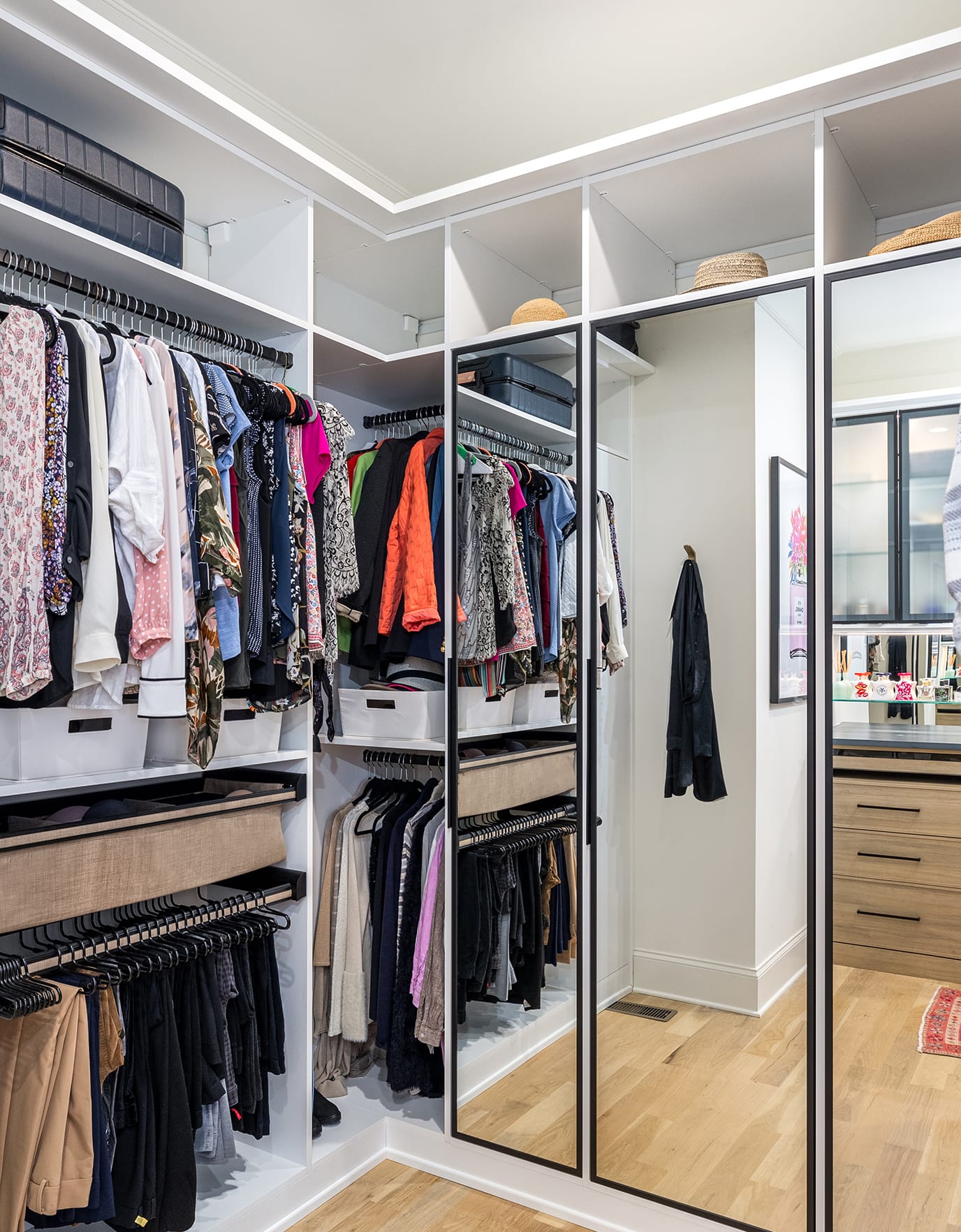 Her walk in closet with open shelves and mirrored doors in white wood grain finish created by California Closets