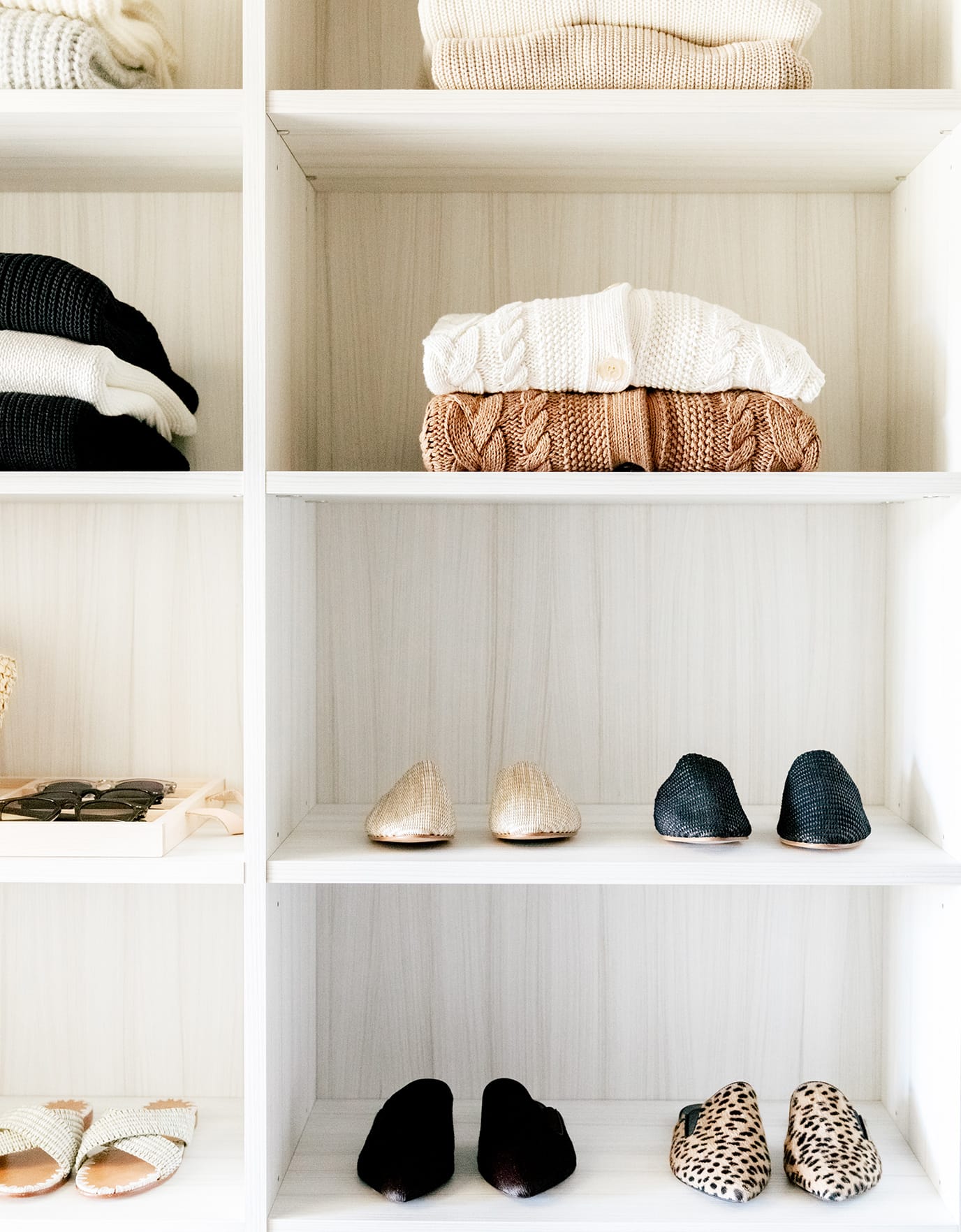 Walk in closet with custom shelving for shoes and sweaters in a neutral wood grain finish by California Closets