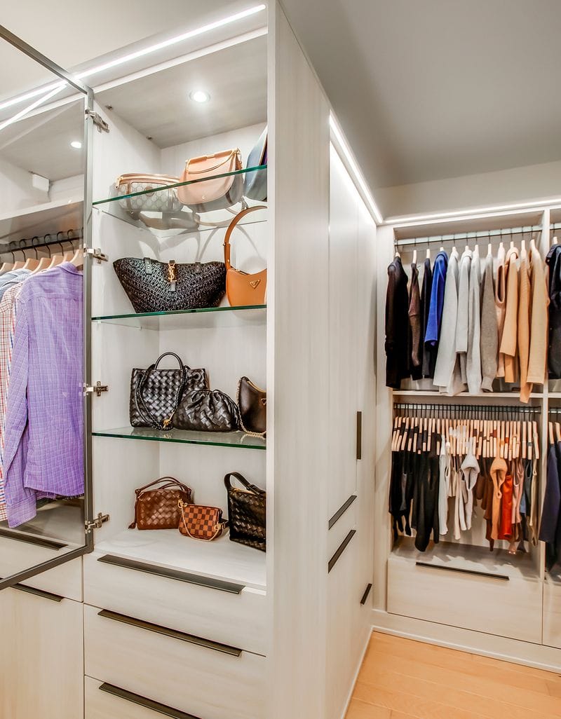 Glass shelving in a walk in closet to store purses with LED lighting created by California Closets
