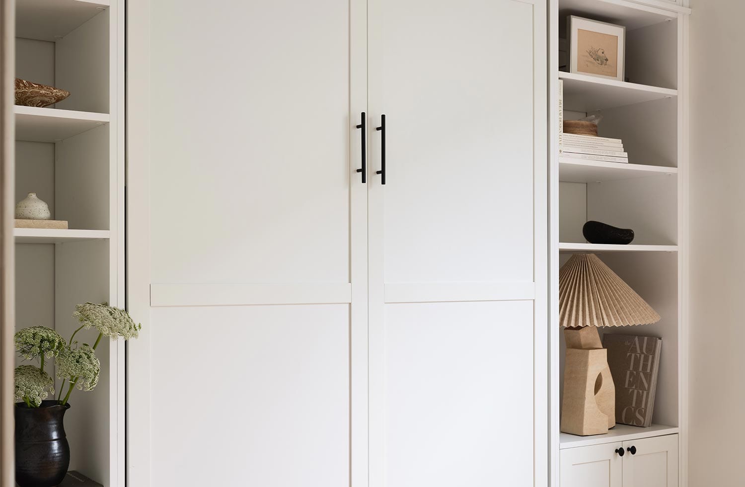 Closed murphy bed with white custom cabinet doors for storage space by California Closets
