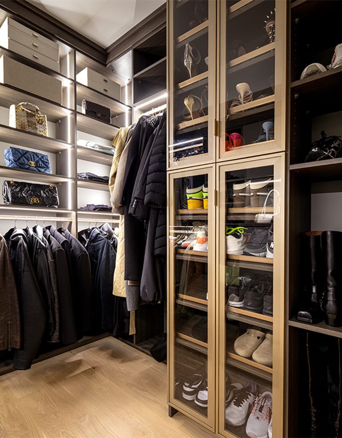 Custom-designed shoe storage with open shelving seen through glass doors in a walk in closet for Ashley Graham from California Closets