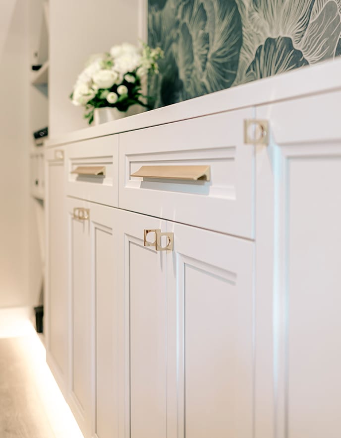 Customized home bar designed with gold hardware, white matte cabinets and glass shelves from California Closets