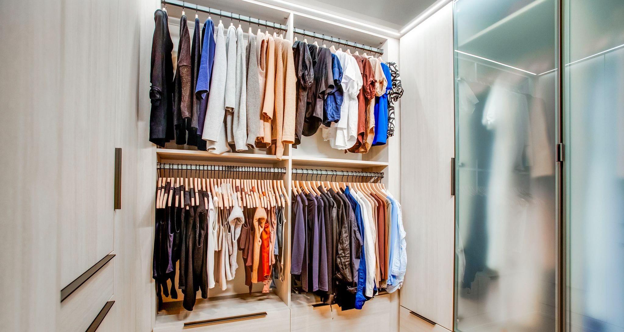 Glass door closet design with wood grain finish and LED lighting created by California Closets