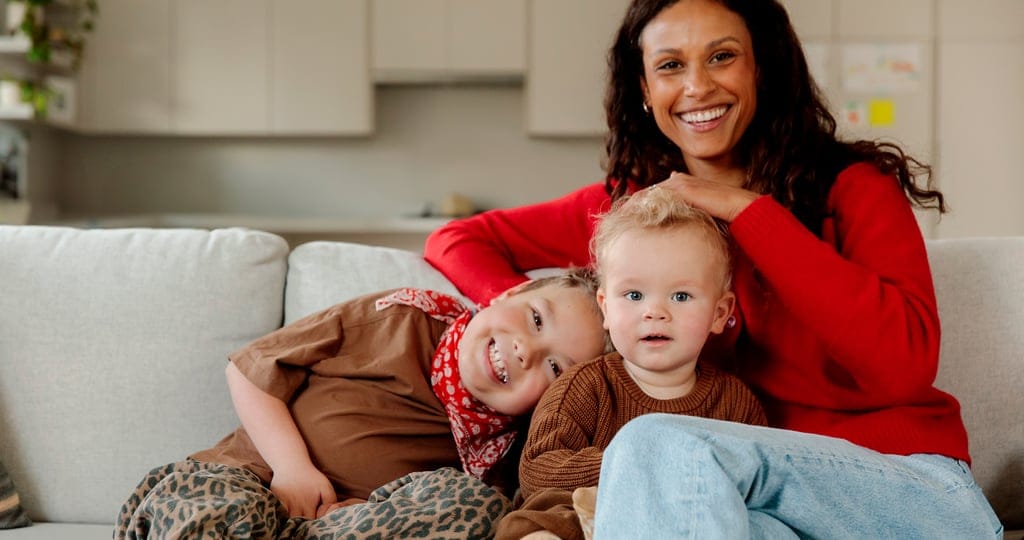 Model Alex Bonnesen sitting on sofa with kids in front of custom storage cabinets from California Closets